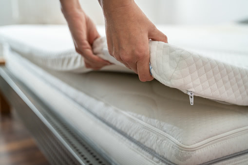 a person holding the corner of a mattress topper